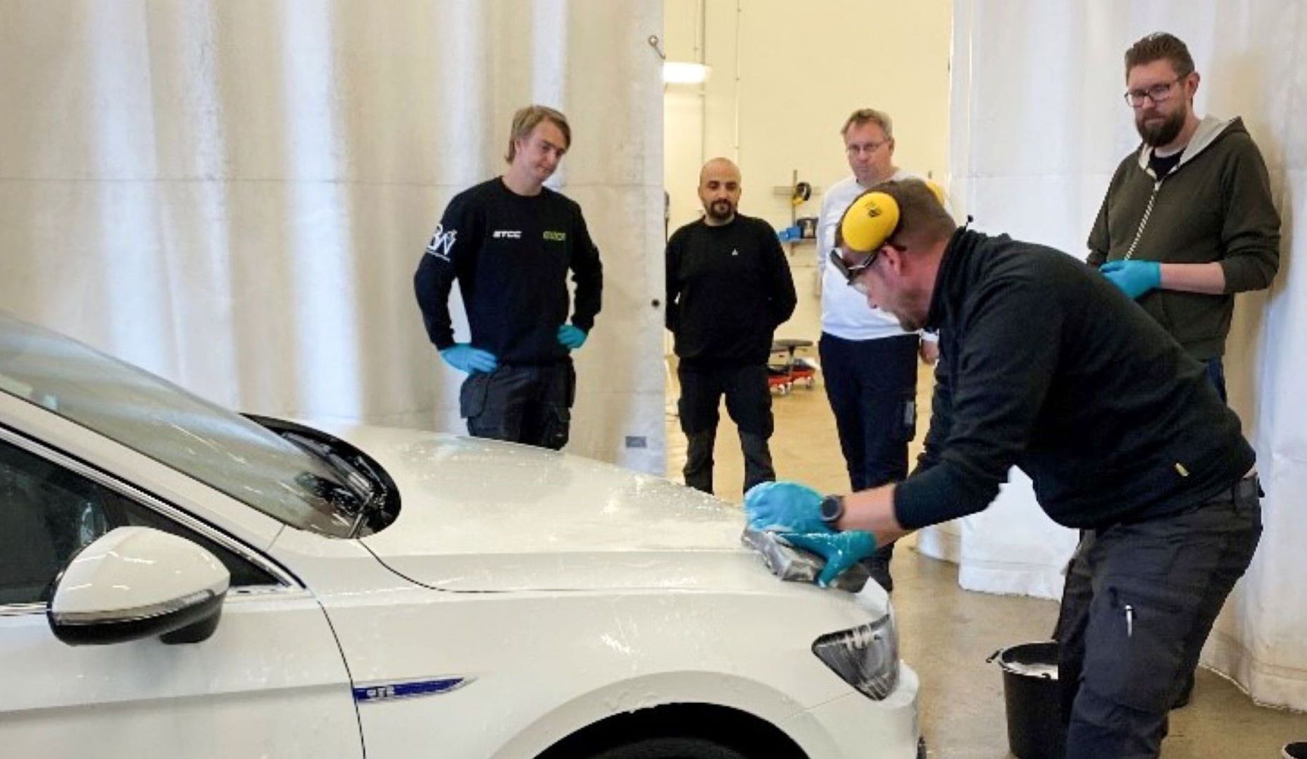 En man som tvättar en bil med 4 personer som tittar på